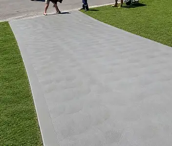 Smooth grey concrete pathway installed alongside green lawn turf